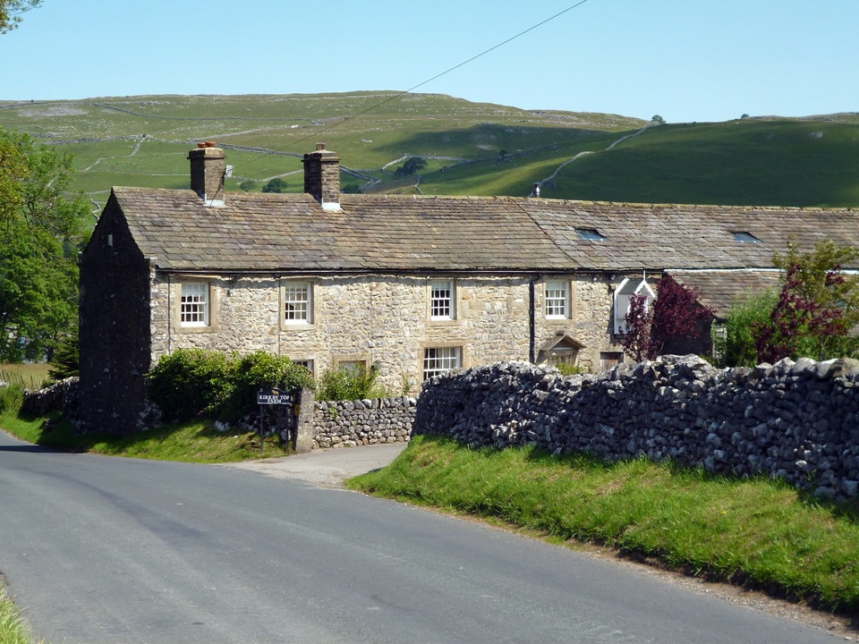 Gritstone cottages with a drystone wall in front and a fell rising behind them in the Yorkshire Dales